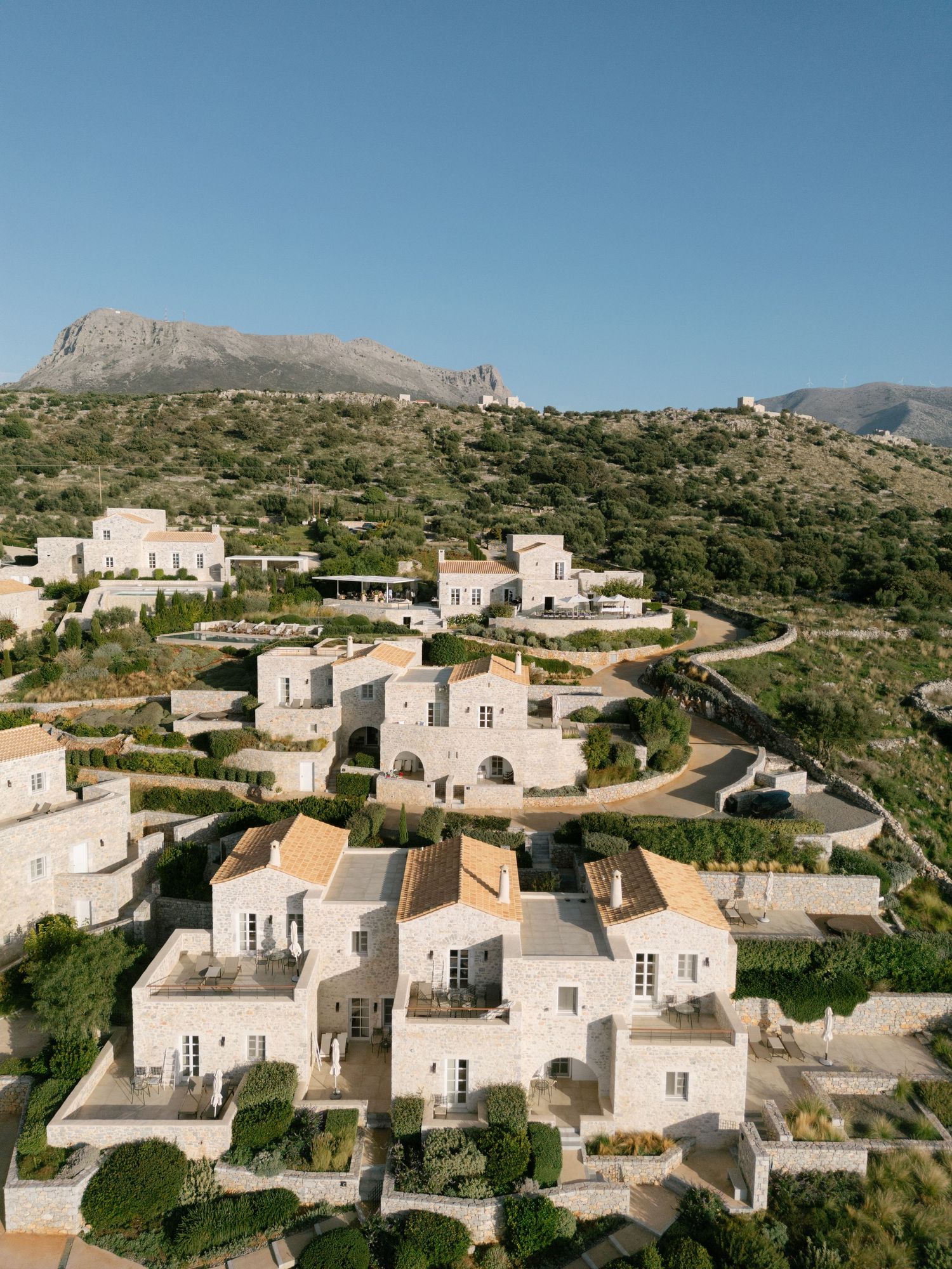 Panoramic view of white Mediterranean hillside villas with terracotta roofs nestled in rugged mountain landscape.