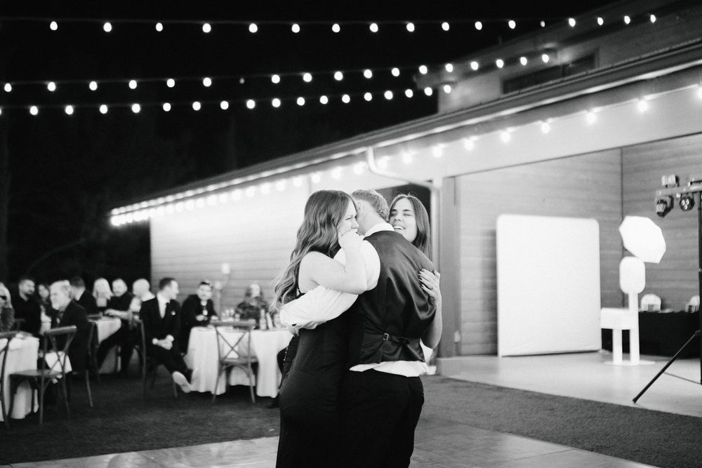 Two brides share a first dance at an outdoor wedding reception with string lights overhead and guests seated in the background.