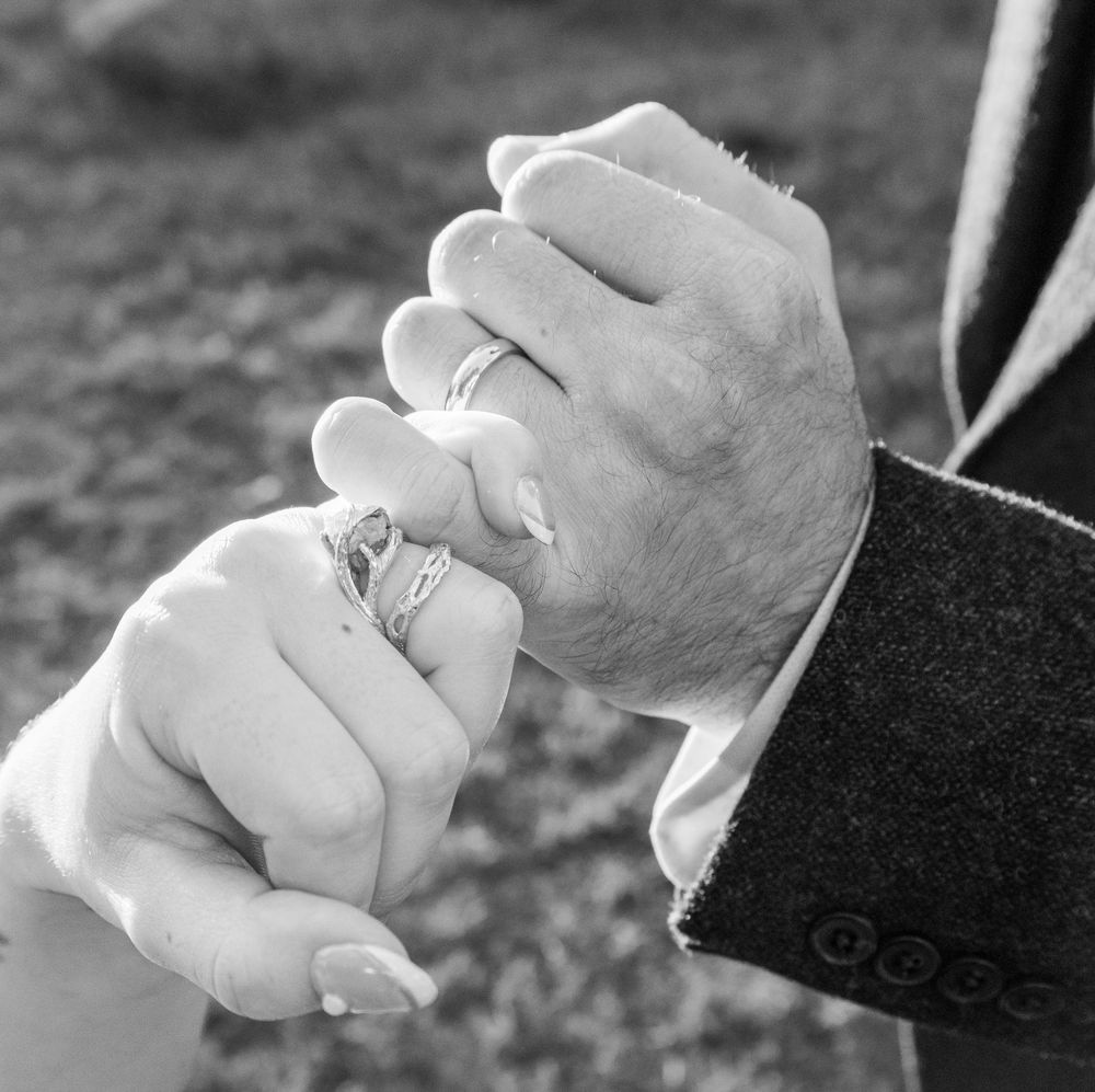 Black and white close-up of newlyweds holding hands, showcasing elegant wedding rings on their fingers.