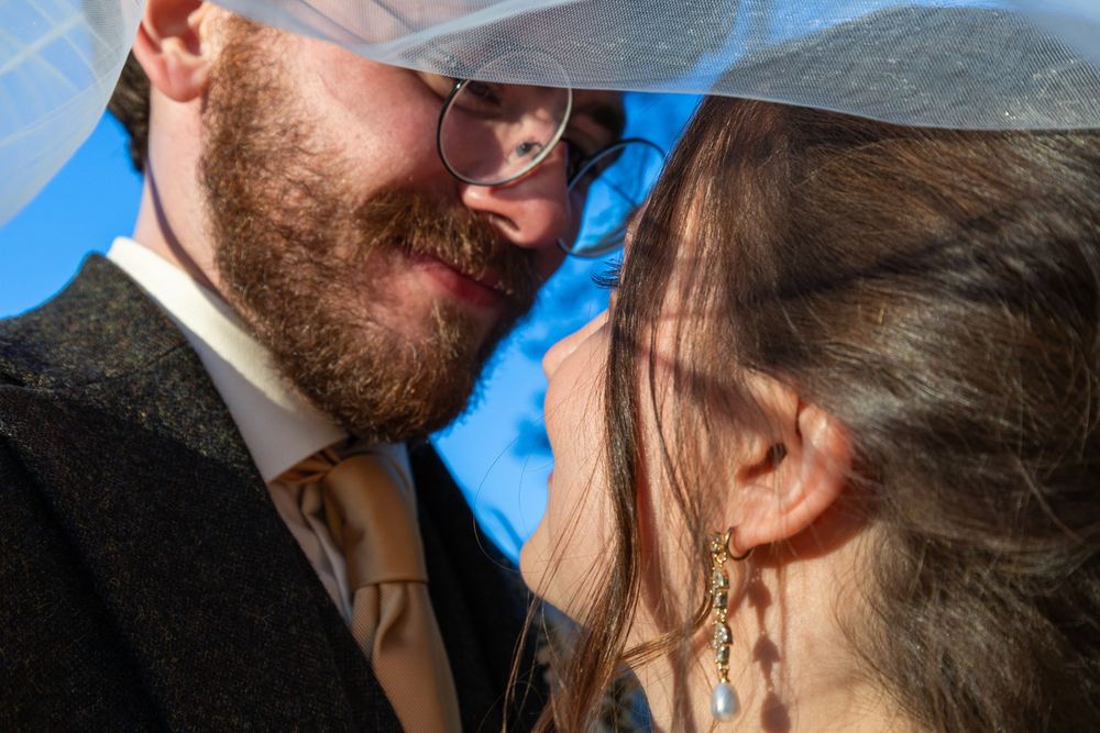 Intimate close-up of a bearded groom and bride sharing a tender moment beneath her wedding veil.