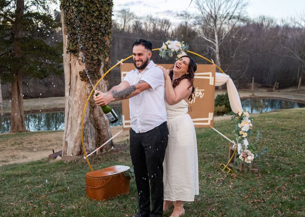 Joyful newlyweds celebrating with champagne by circular floral arch in outdoor wedding ceremony.