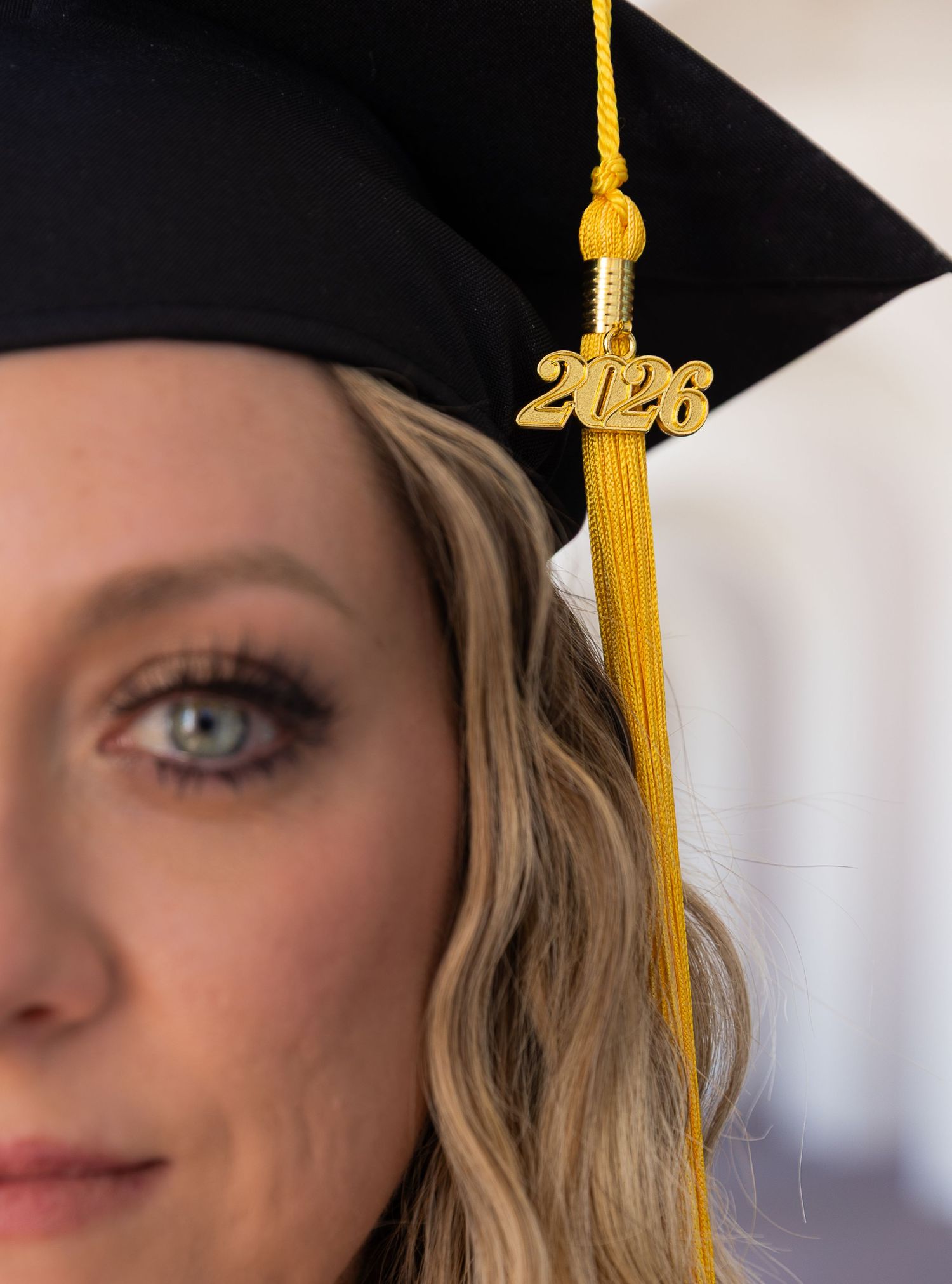 Close-up of a woman wearing a black graduation cap with a gold 2026 tassel, celebrating her upcoming graduation.
