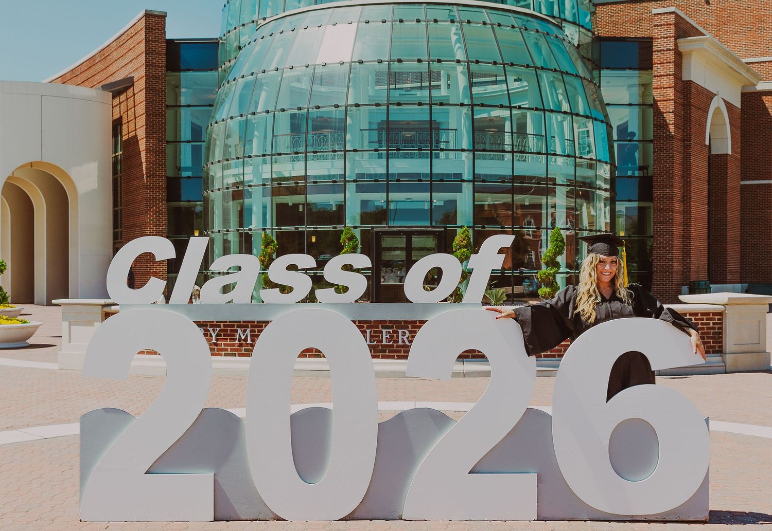 Student poses beside a large Class of 2026 sign in front of a modern university building.