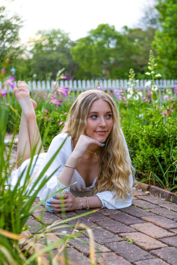 Blonde woman lying on brick path surrounded by colorful garden flowers.