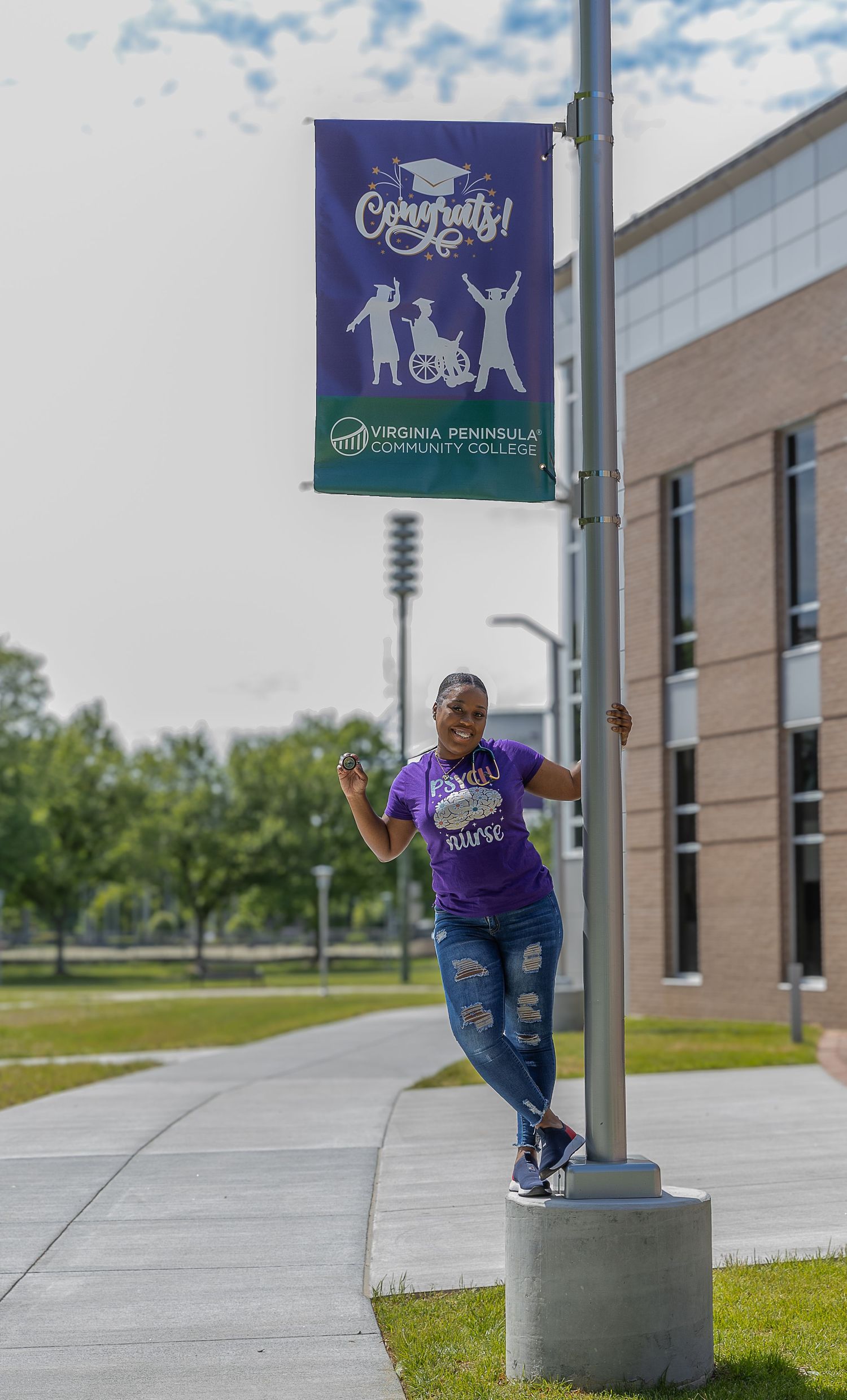 A smiling graduate poses by a Virginia Peninsula Community College Congrats banner on campus.