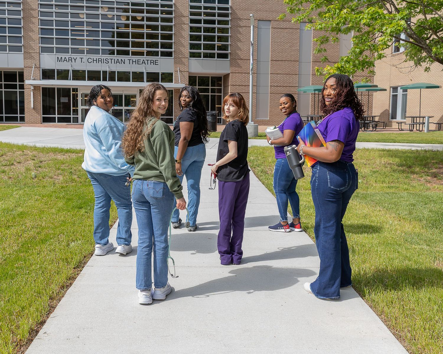 Diverse group of college students gathered on campus walkway outside modern university building on sunny day.
