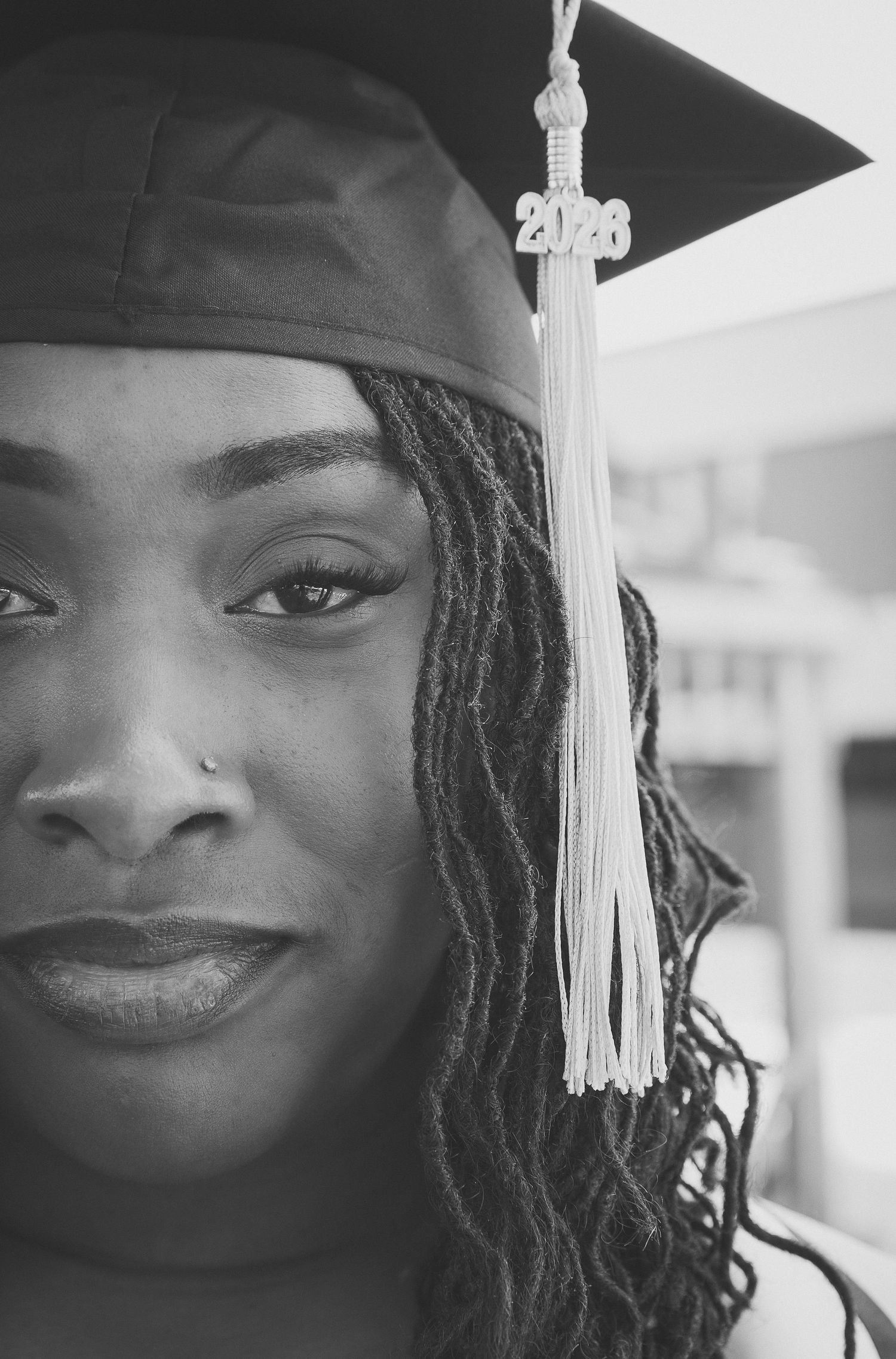 Black and white portrait of a young woman wearing a 2023 graduation cap with tassel and locs hairstyle.