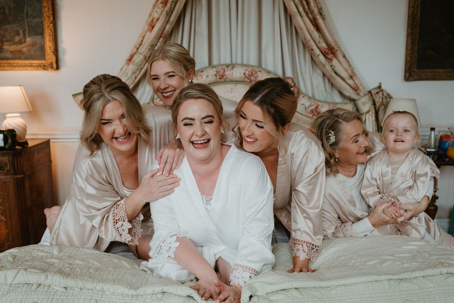 A group of people wearing white robes share joyful moments while lounging together on a bed at Hooton pagnell hall