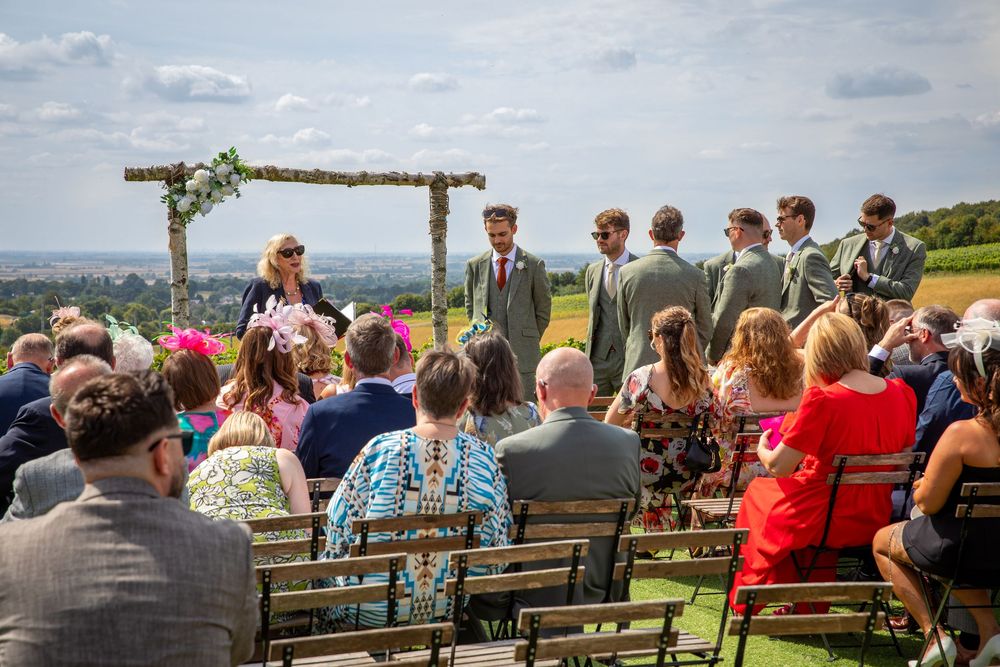 Outdoor wedding ceremony with guests seated on wooden benches overlooking stunning countryside panoramic view.