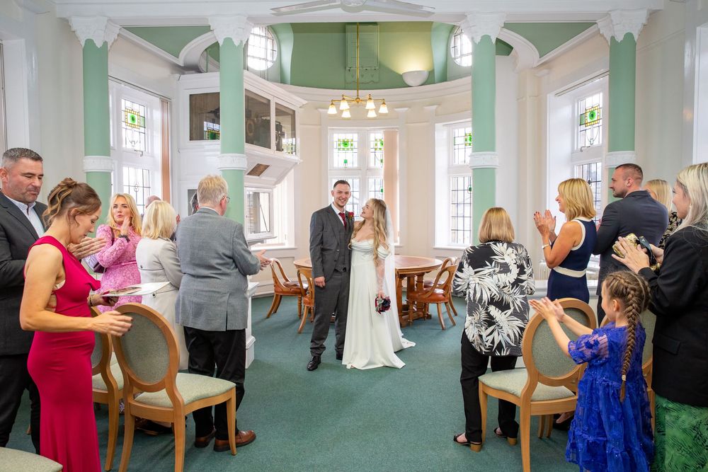 Wedding ceremony moment as bride and groom stand at altar while guests applaud in elegant green and white venue.