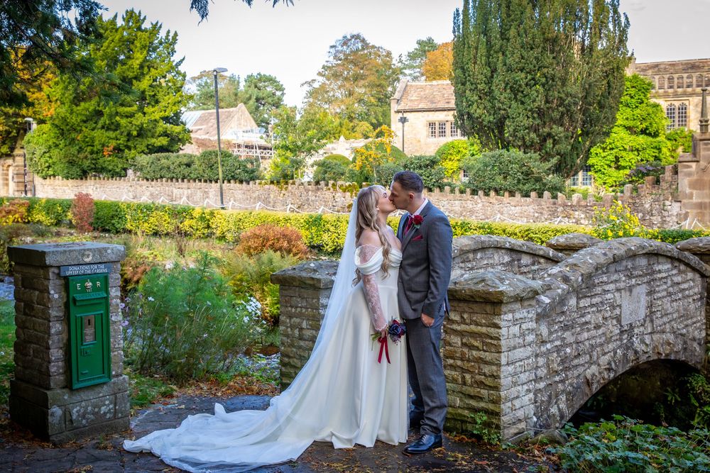 Bride and groom share romantic kiss on stone bridge surrounded by lush autumn garden greenery.