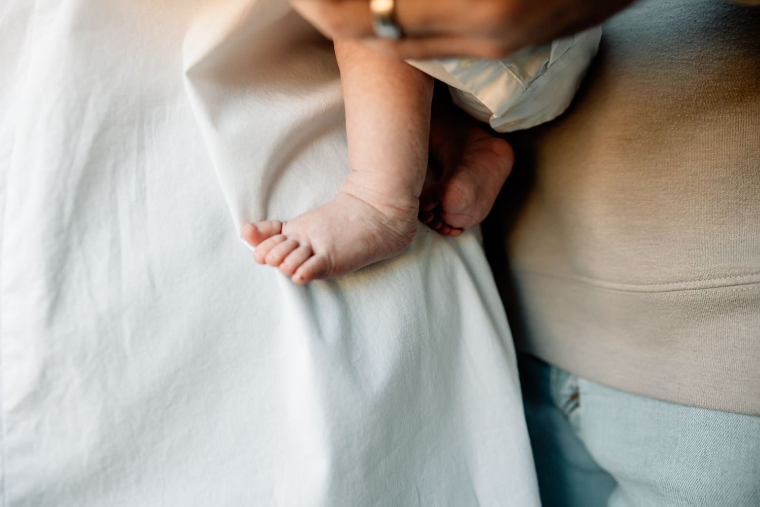 Close-up of a newborn baby's tiny feet resting on a soft white blanket beside a parent.