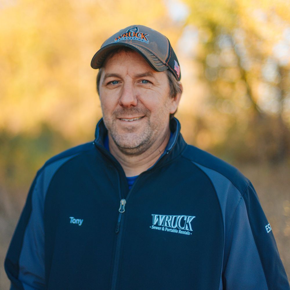 Man named Tony wearing a Wruck company jacket and baseball cap smiling outdoors in autumn setting.