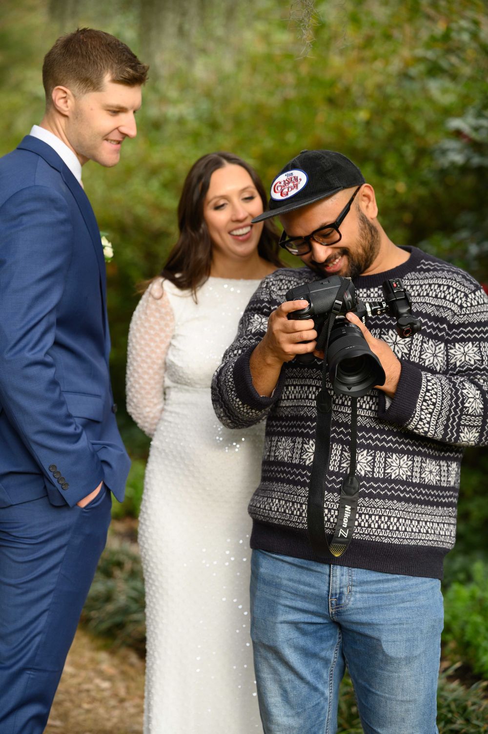 A wedding photographer shows a couple their photos on a camera display in an outdoor garden setting.