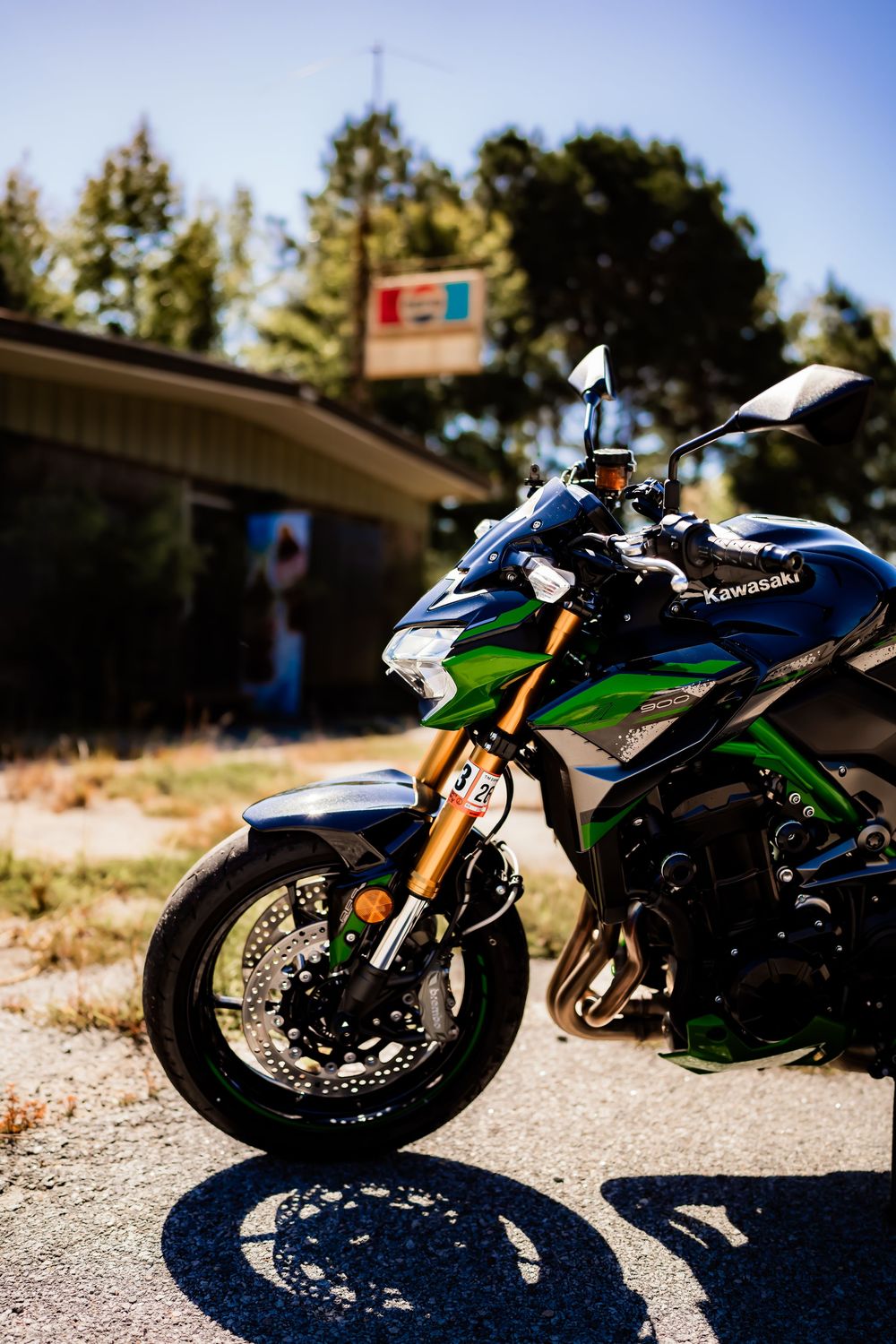 Green and black Kawasaki sport motorcycle parked on pavement near an abandoned building with trees in background.