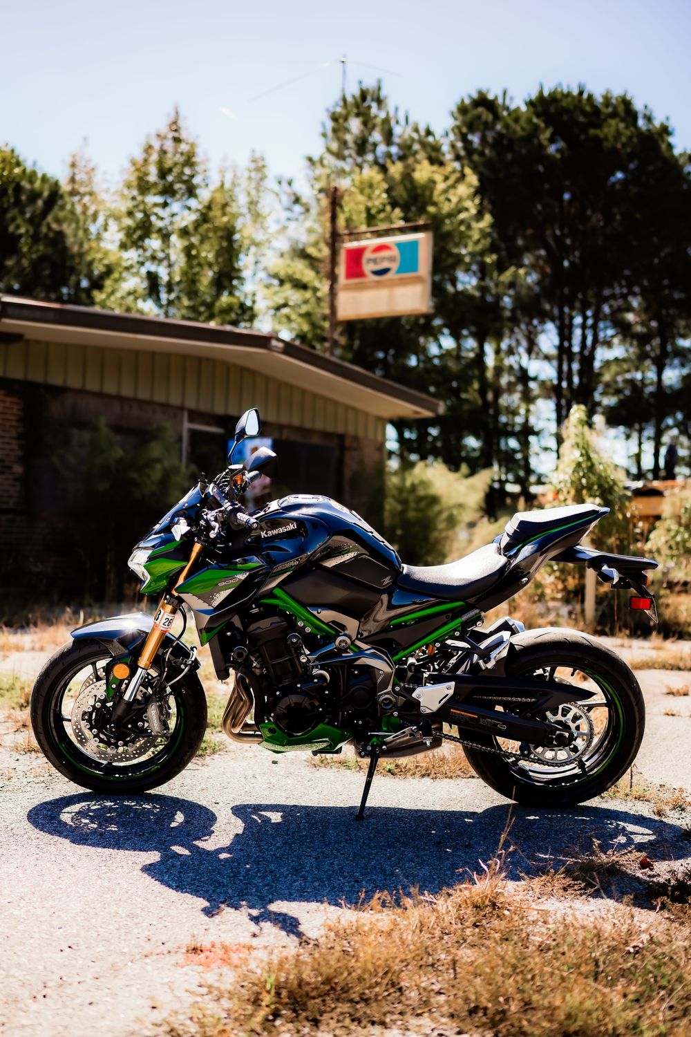 Green and black Kawasaki sport motorcycle parked outside a vintage building with a Pepsi sign.