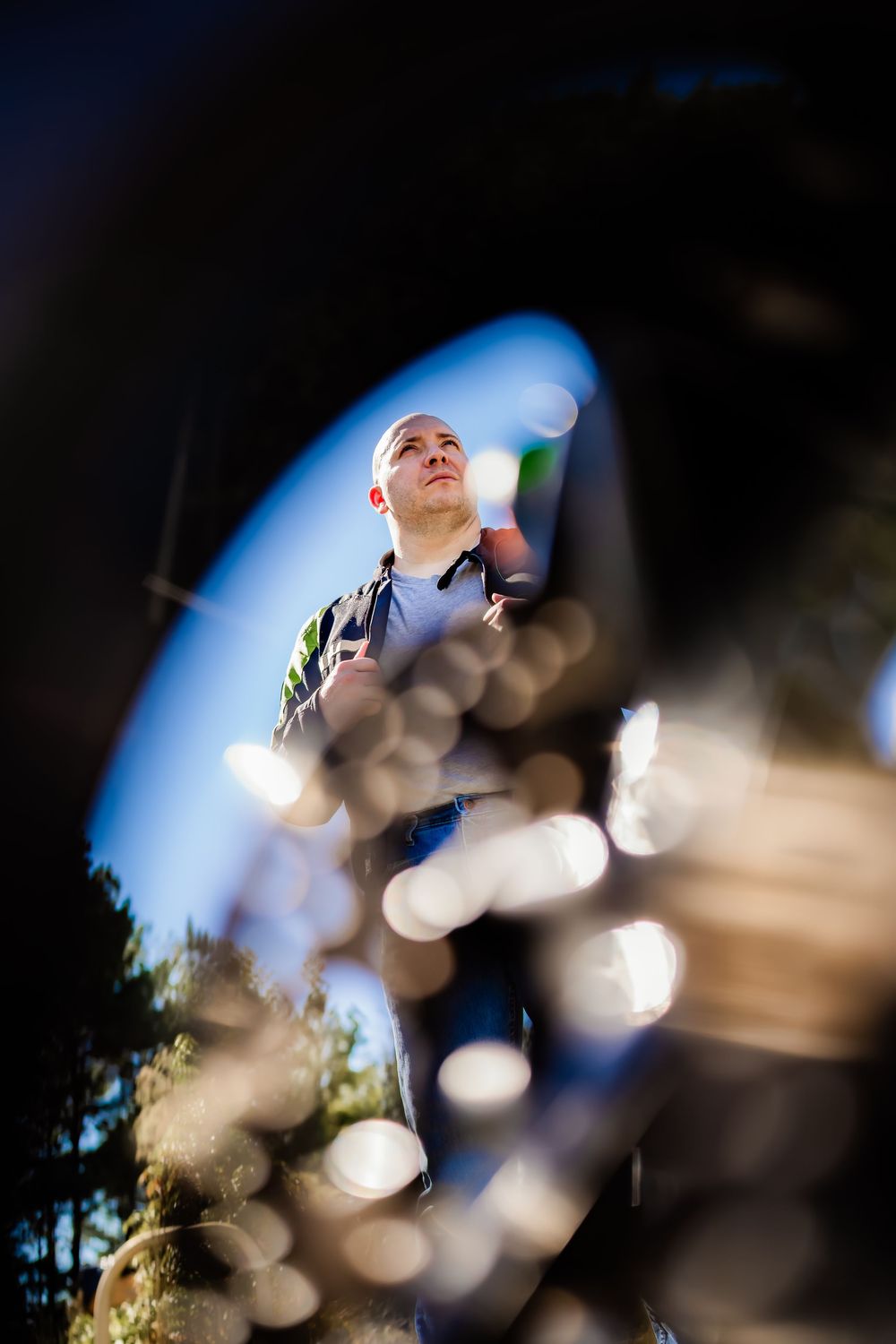 Bald man viewed through motorcycle wheel spokes with bokeh light effects outdoors.
