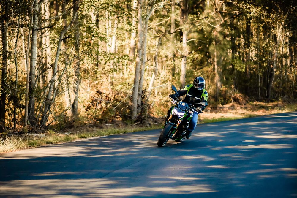 Motorcyclist leaning into a curve on a scenic forest road during autumn, surrounded by golden trees.