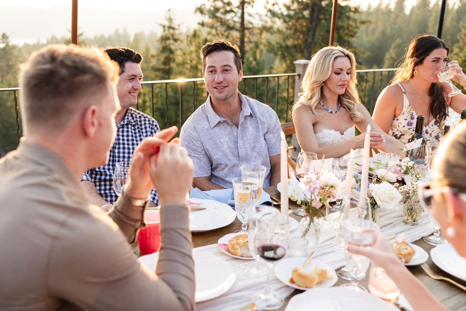 Friends laughing and celebrating at an elegant outdoor wedding reception dinner table at sunset.