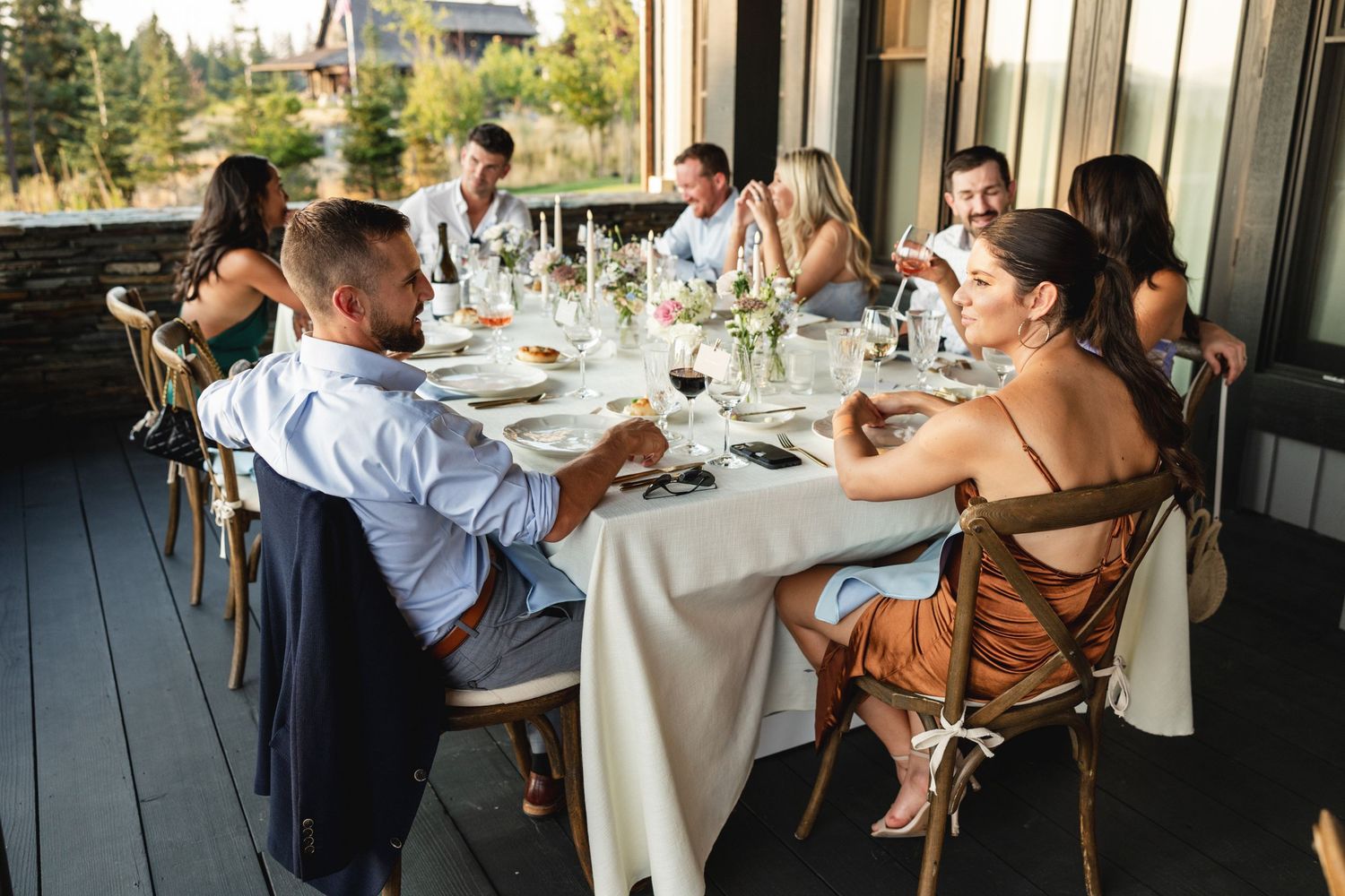 Group of elegantly dressed friends enjoying a dinner party on a sunlit outdoor patio.
