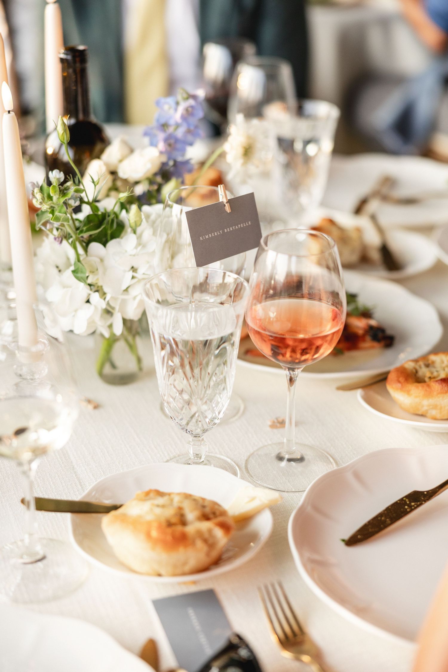 Elegant wedding table setting with rose wine, crystal glassware, white florals, and place cards.