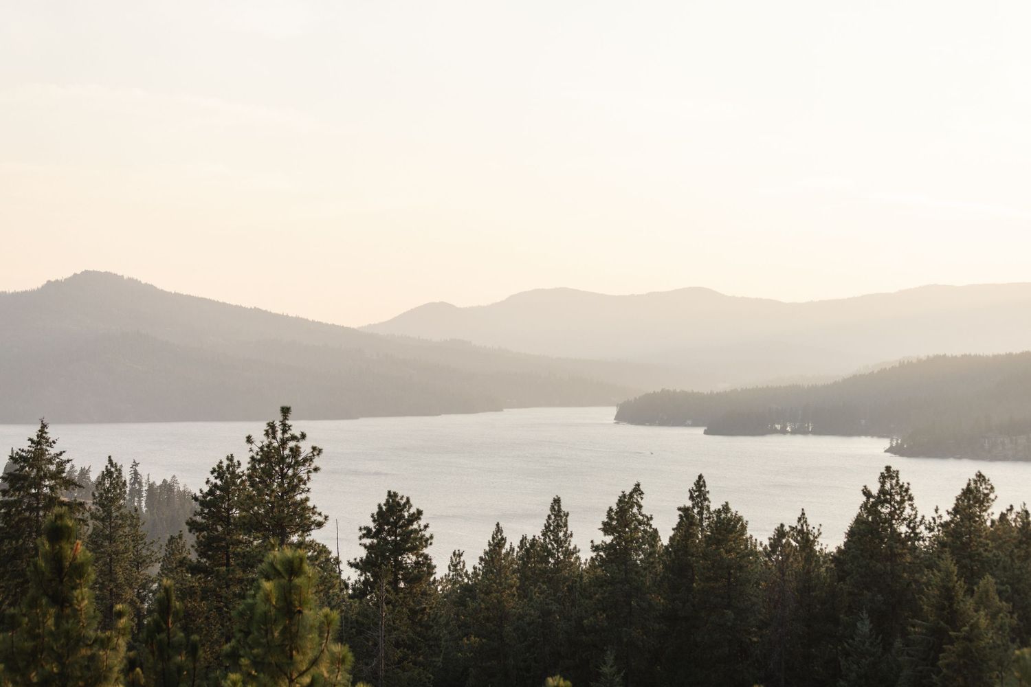 Serene panoramic view of a mountain lake surrounded by pine forests in soft evening light.
