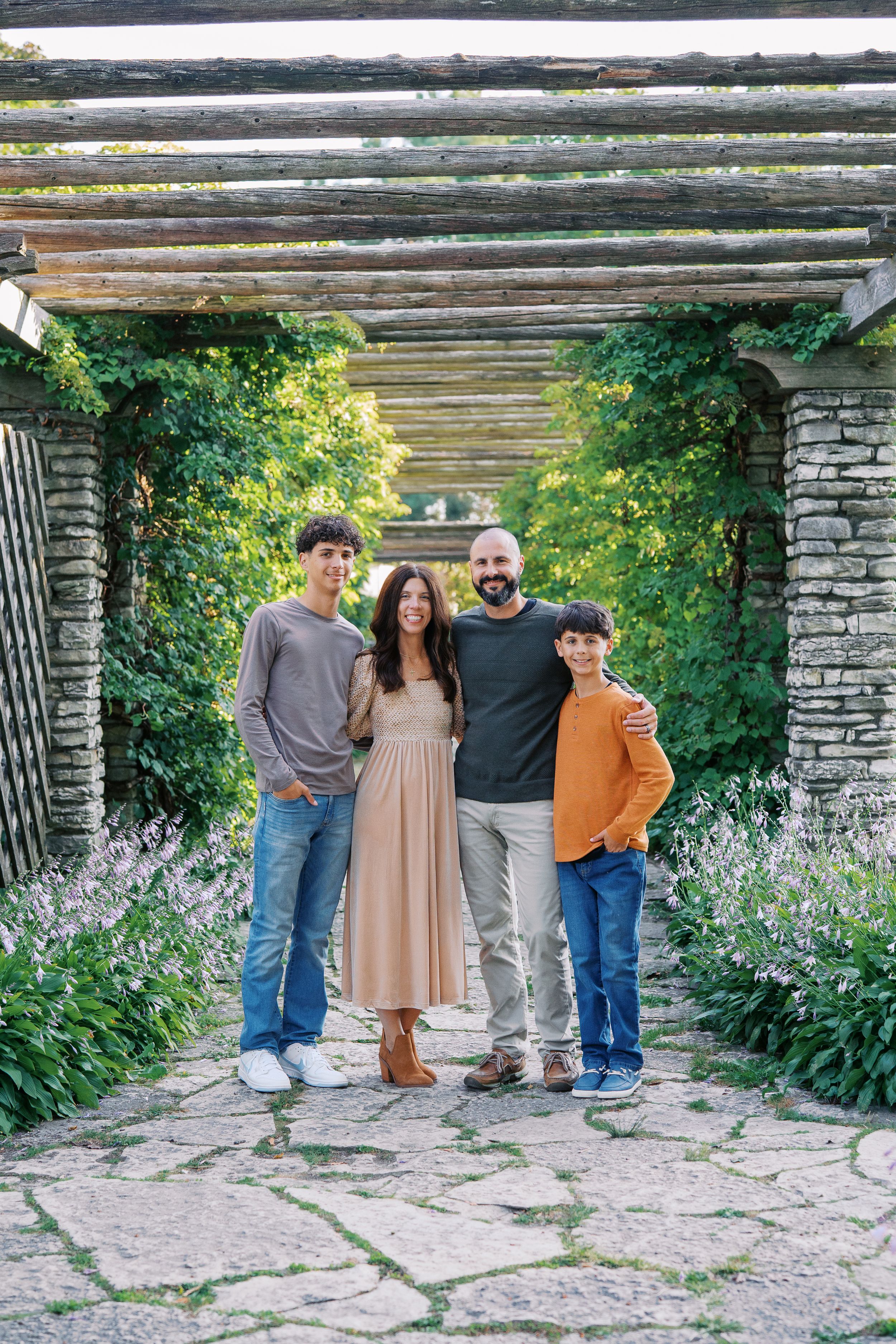 A group poses together under a rustic wooden pergola with stone pillars and lavender plants in the foreground.