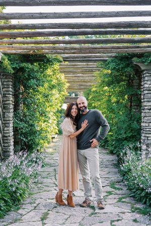 A couple shares a romantic moment in a garden setting with stone walls and blooming yellow flowers.