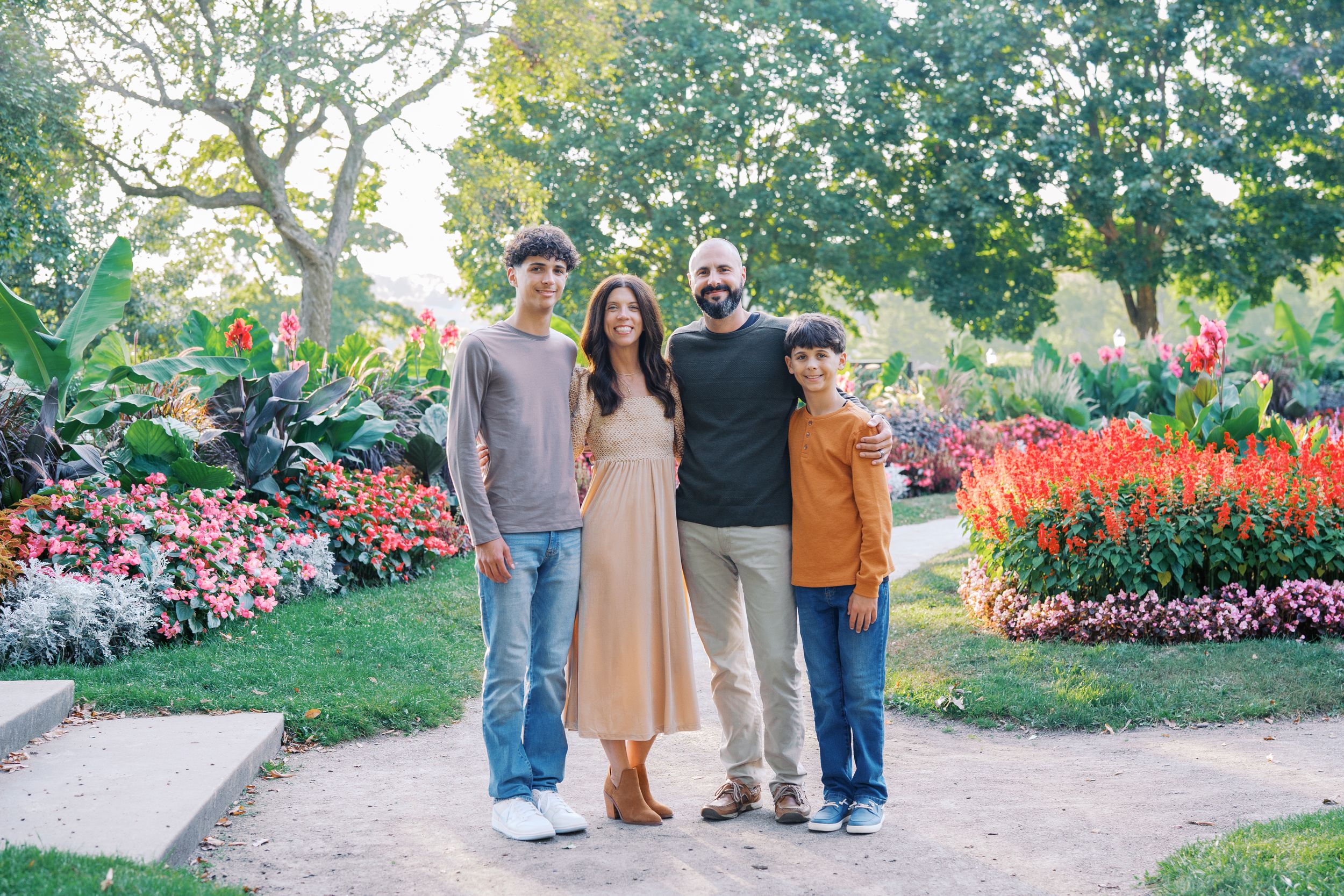 A group of people stand together in a garden with blooming red flowers and lush greenery in the background.