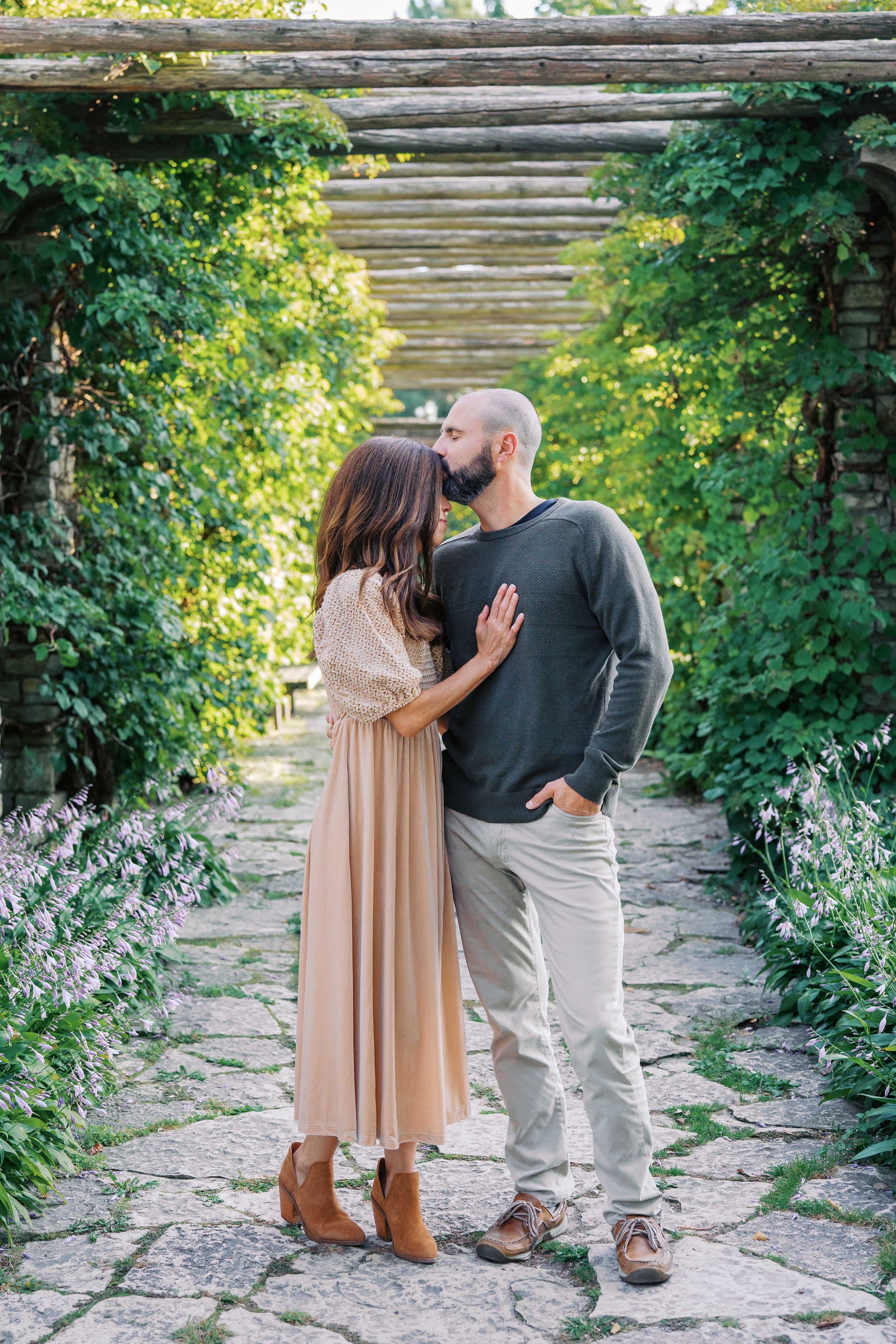Romantic couple poses together on stone steps surrounded by lush green foliage.