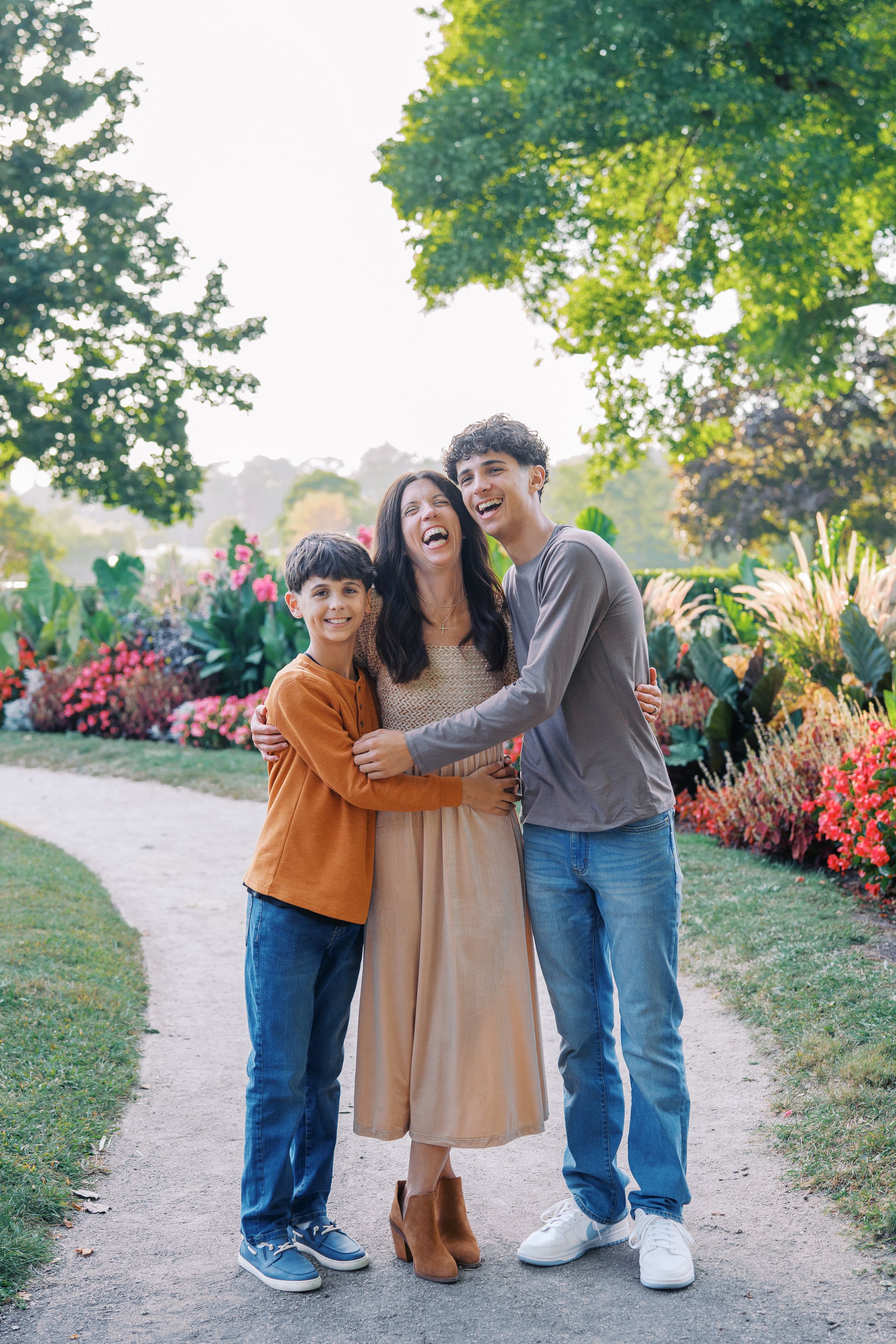 A joyful family moment captured on a garden path surrounded by vibrant red flowers and lush greenery.