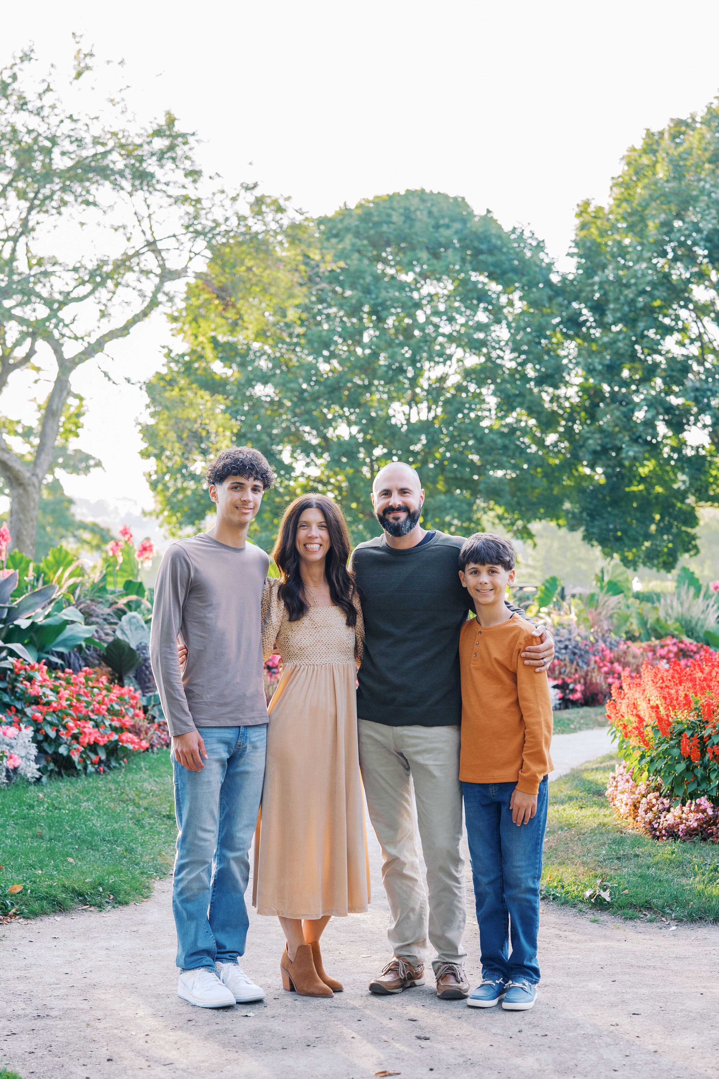 A group poses together in a garden setting with vibrant red flowers and greenery during golden hour.