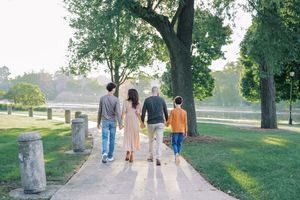 A family walks together on a tree-lined path in a park during a sunny autumn day.
