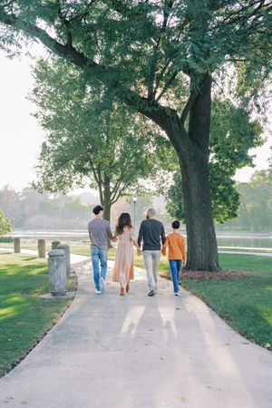 A group of people walking together on a peaceful path under a large shady tree in a park on a sunny day.