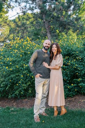 A couple shares a joyful moment together in front of yellow wildflowers and greenery on a sunny day.