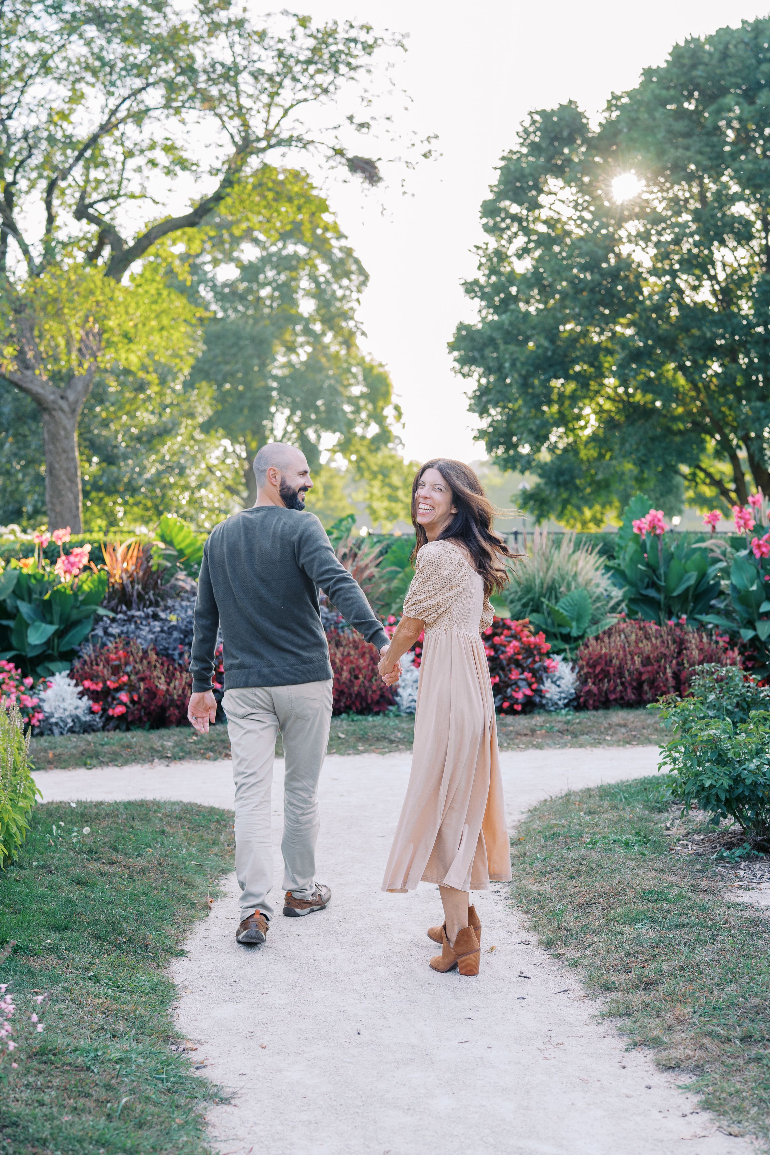 Couple strolling along winding garden path surrounded by colorful landscaping and trees.