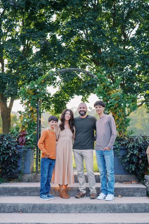 Family group poses casually together on stone wall with garden backdrop.