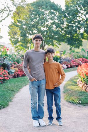 Two people walk together on a garden path surrounded by colorful flowers and lush greenery on a sunny day.