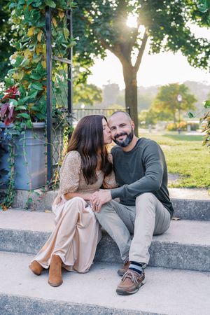 Couple sitting close together on concrete ledge sharing intimate moment in outdoor garden setting.
