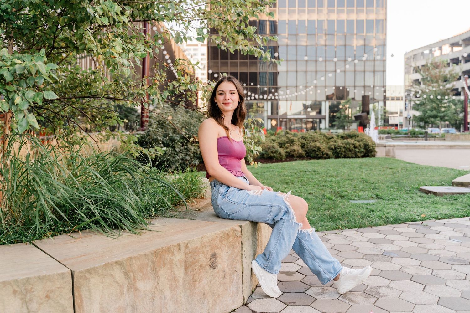 Perrysburg High School senior in a muted pink tank top and jeans sits casually on a concrete ledge in an urban garden in Downtown Toledo.