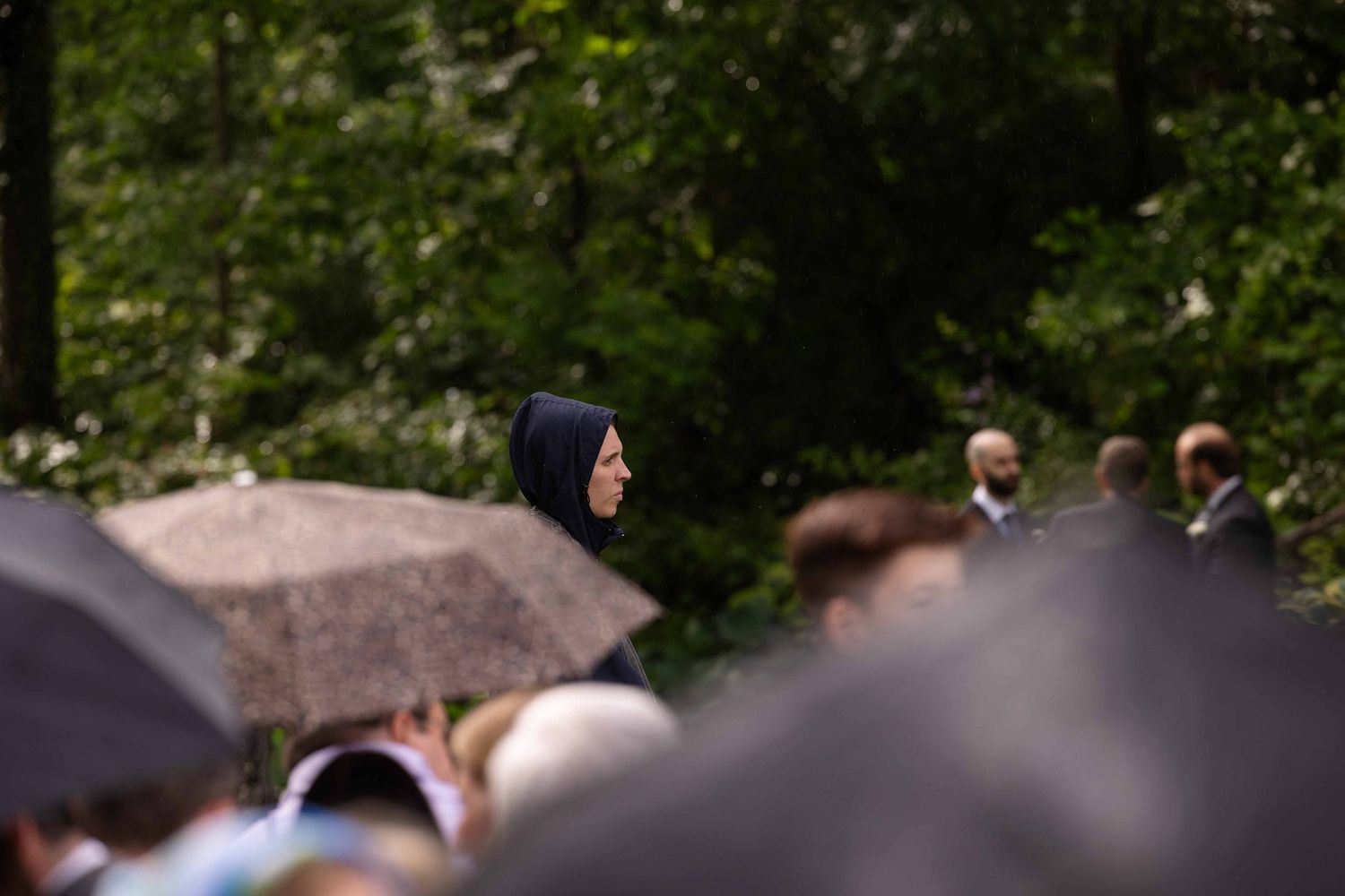 Spectators gather in a wooded area to watch an outdoor event on a sunny day.