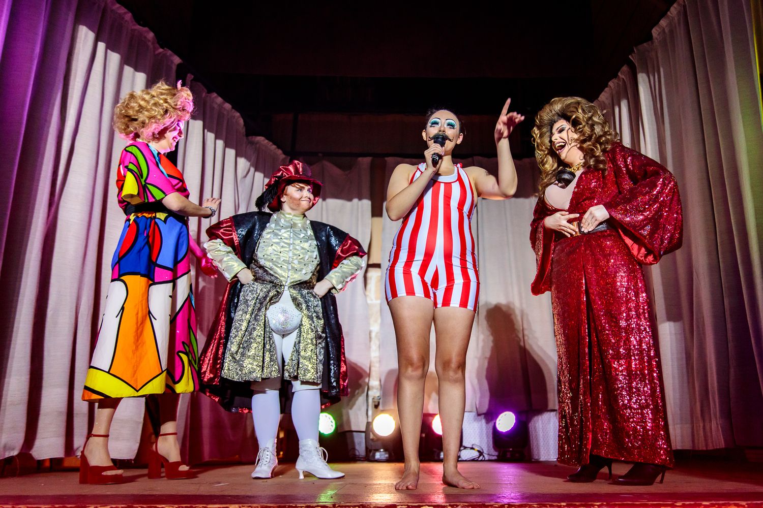 Performers in colorful costumes pose together on stage during a theatrical production.