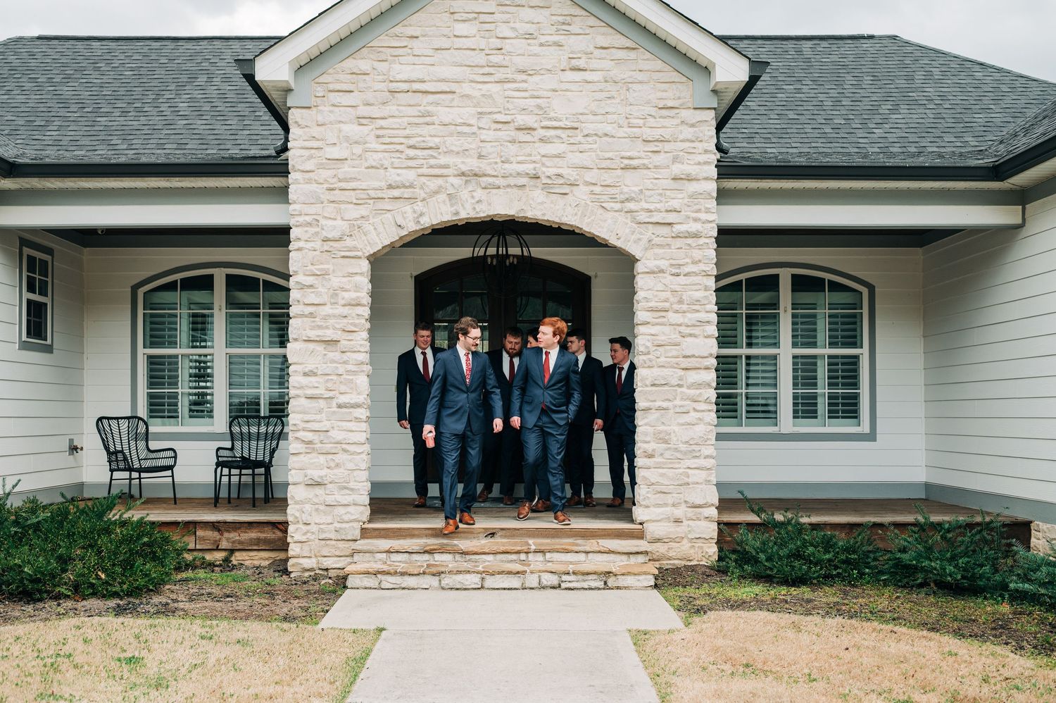 A group of formally dressed people stand in front of a modern stone and white siding house exterior.