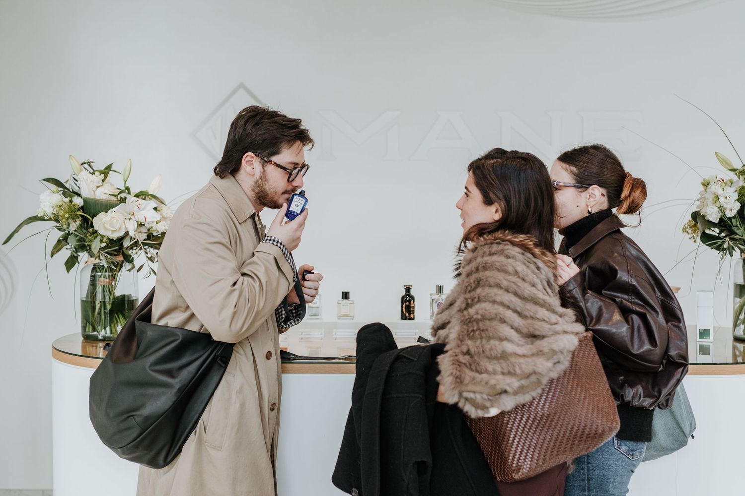 Two people in winter coats embrace in a light and airy indoor setting with white walls and minimal decor.