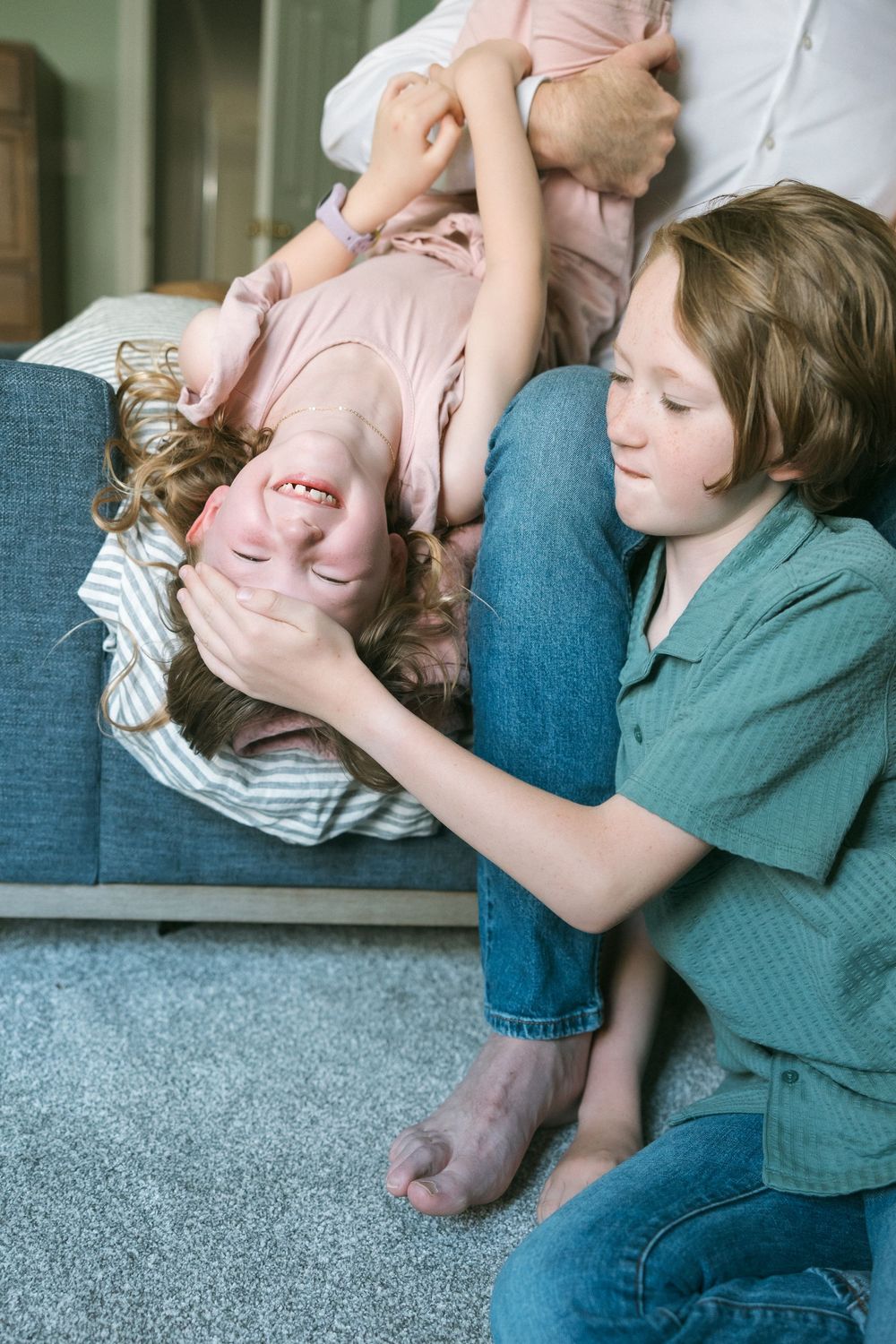 Two children playfully wrestling on living room floor near couch, laughing and enjoying sibling bonding time.