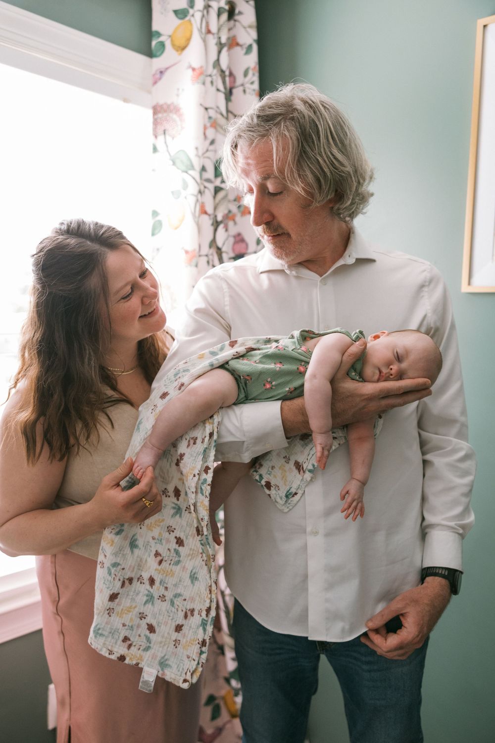 New parents lovingly admire their sleeping newborn baby wrapped in blanket in decorated nursery room.