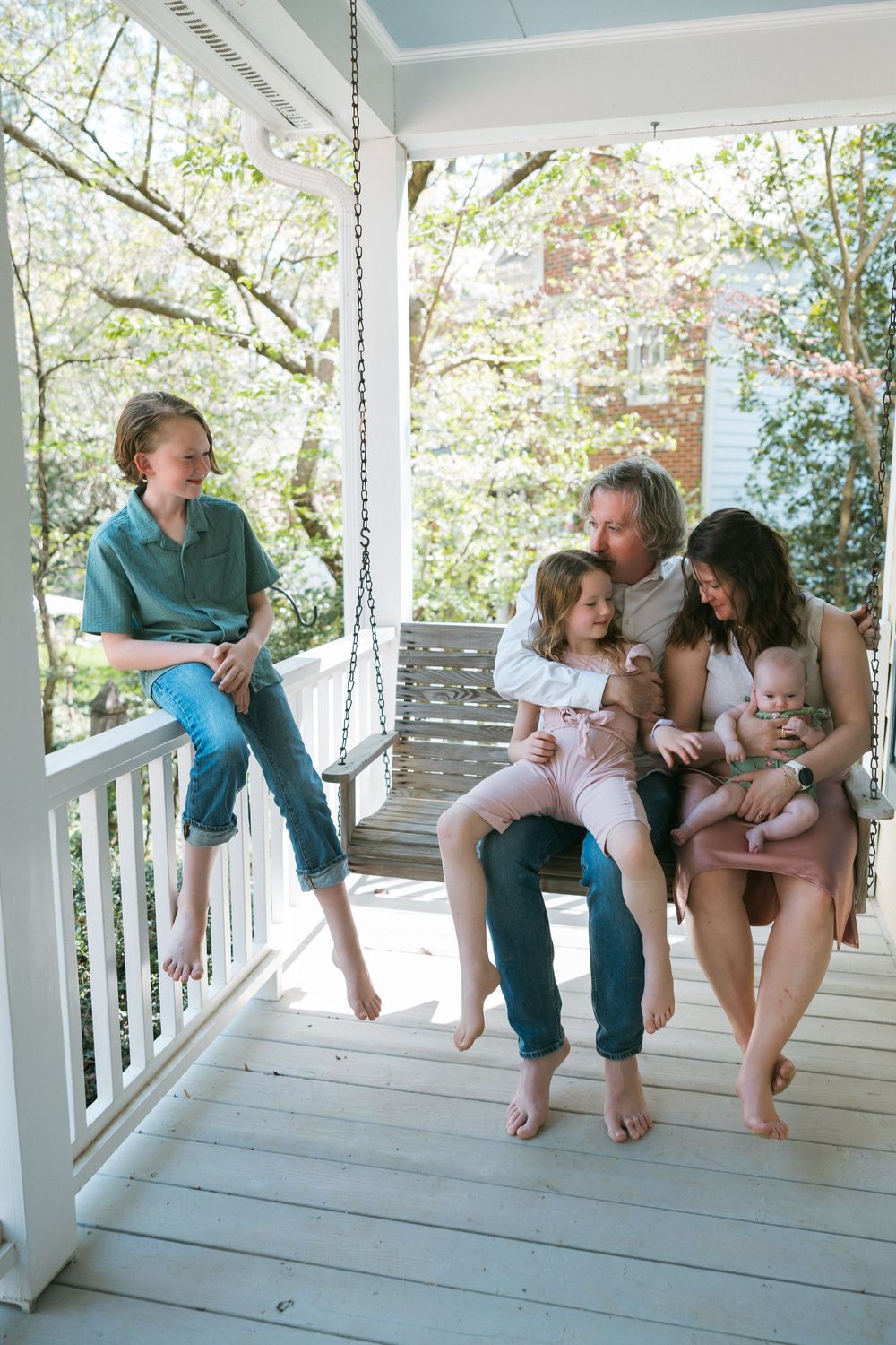 Family of five relaxing on a white porch swing surrounded by spring blooms.