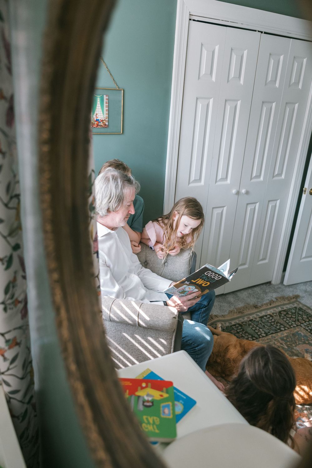 Grandmother and granddaughter reading a book together on the floor beside a closet, viewed through a gold-framed mirror.