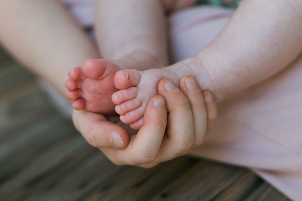 Close-up of adult hands gently cradling tiny newborn baby feet, symbolizing love and new parenthood.