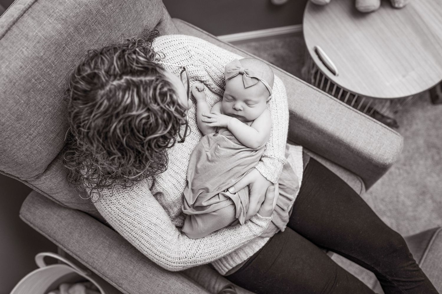 Black and white overhead photo of a mother cradling her sleeping newborn baby in a cozy armchair.